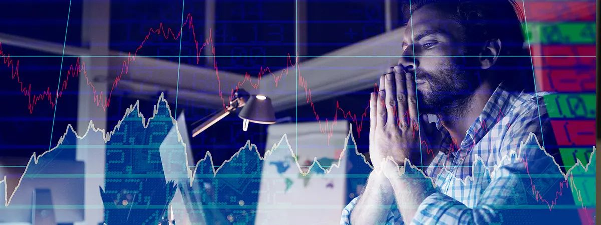 Un hombre reflexiona ante una computadora mientras observa gráficos de datos financieros.