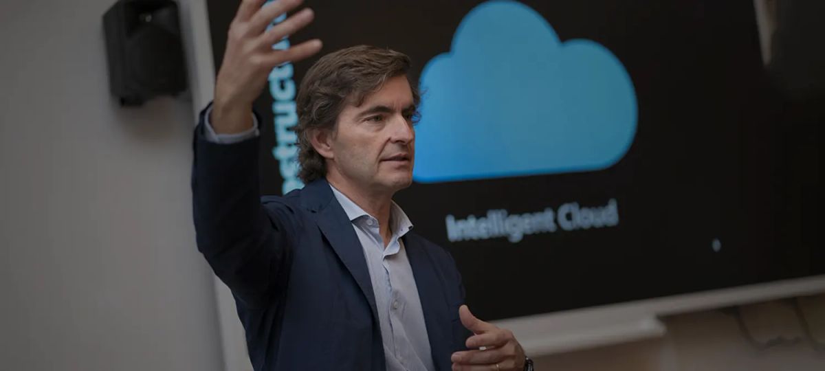 Un hombre está presentando con entusiasmo frente a una pantalla que muestra un logo de nube.
