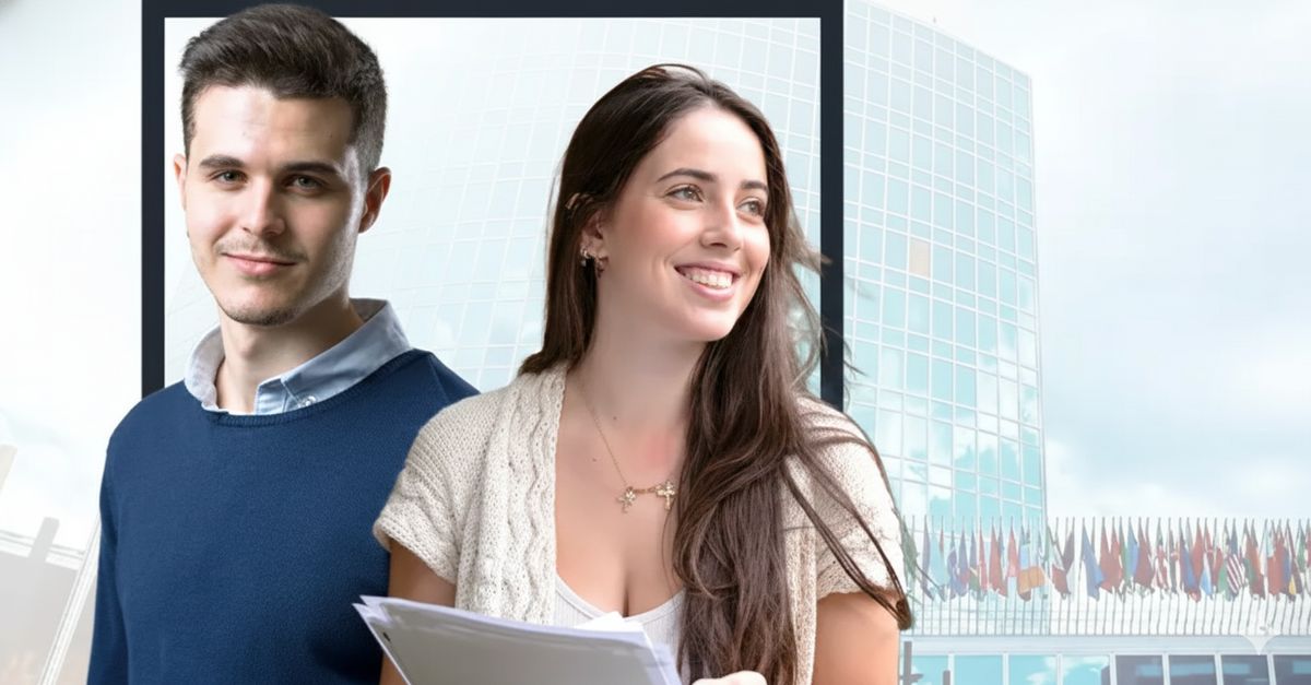 Dos jóvenes posan sonrientes frente a un edificio moderno con banderas al fondo.