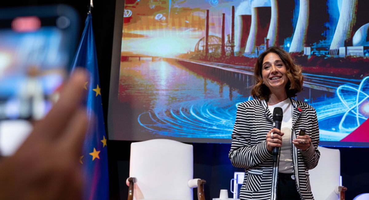 Una mujer sonriente habla en un evento mientras se proyecta una imagen de un paisaje industrial de fondo.