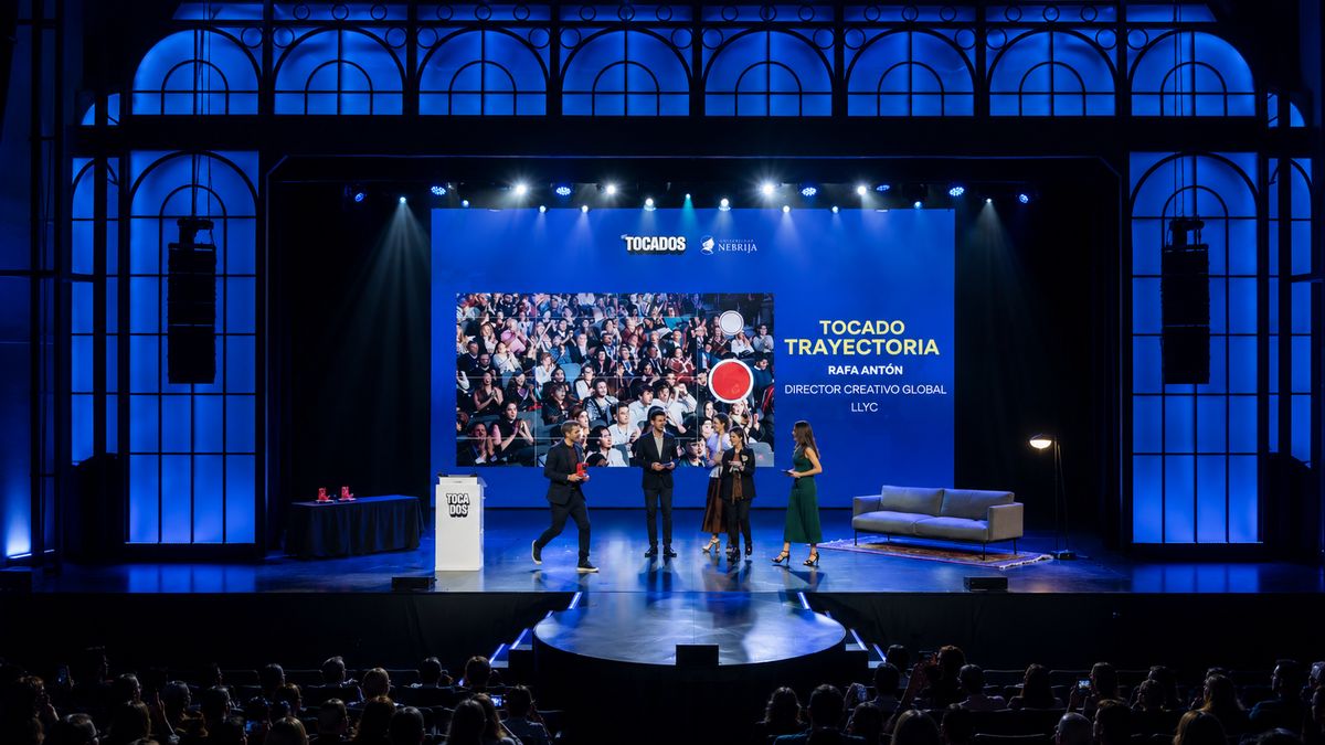 Un grupo de personas en un escenario durante un evento, con una presentación visual de fondo que muestra una multitud.