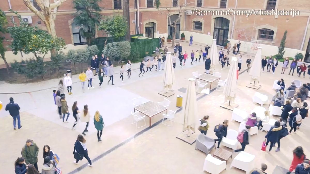 Un grupo de personas camina en un patio con mesas y sillas al aire libre.
