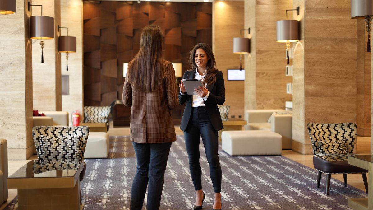 Dos mujeres conversan en el vestíbulo elegante de un hotel.