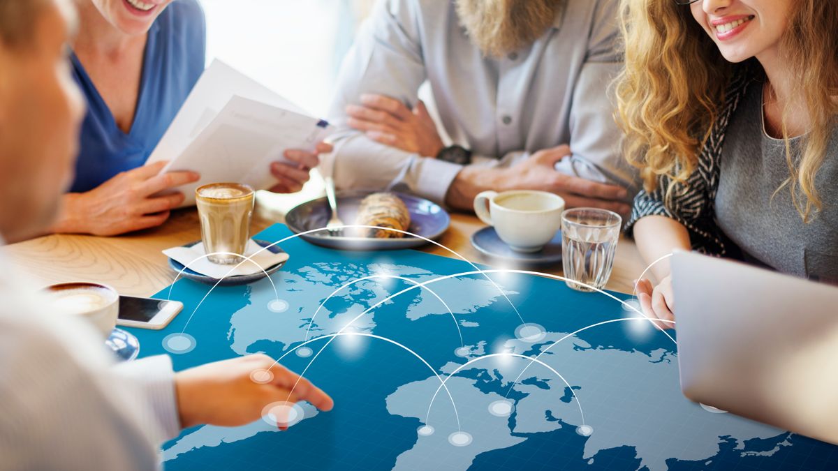 Un grupo de personas se reúne en una mesa con un mapa del mundo proyectado y varias tazas de café.