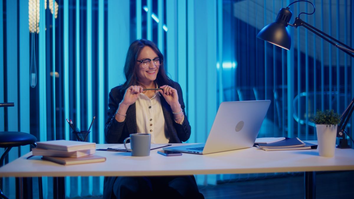 Una mujer sonriente trabaja en su computadora portátil en un ambiente moderno y luminoso.