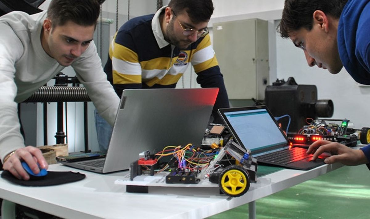 Tres personas trabajan en un proyecto de robótica en una mesa con computadoras y un robot.
