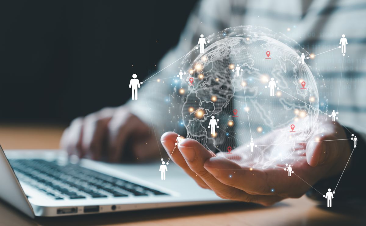 Una persona sostiene un globo terráqueo digital mientras trabaja en una computadora portátil.