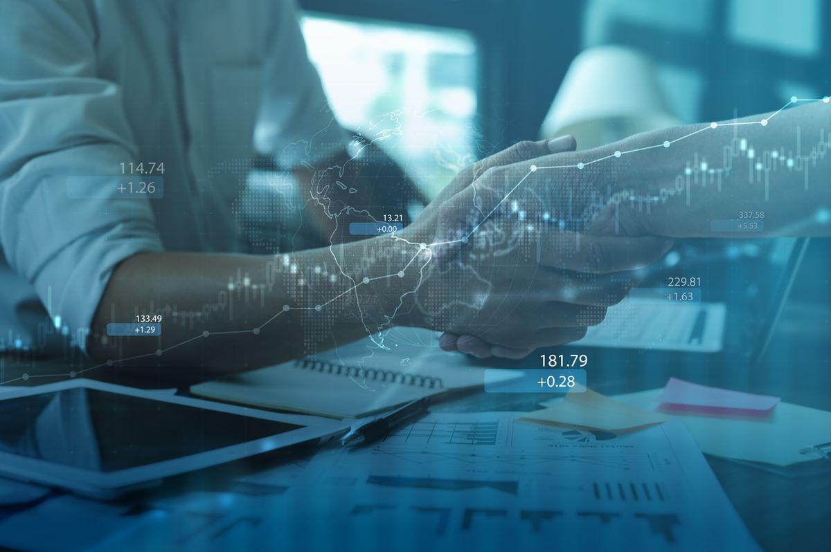Dos personas se estrechan la mano en un entorno de negocios con gráficos y datos financieros de fondo.