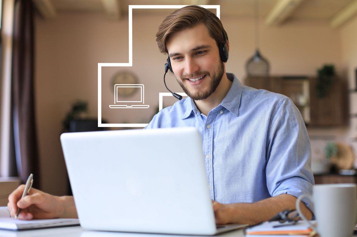 Un hombre sonriente utiliza una computadora portátil mientras lleva auriculares y trabaja en un ambiente acogedor.