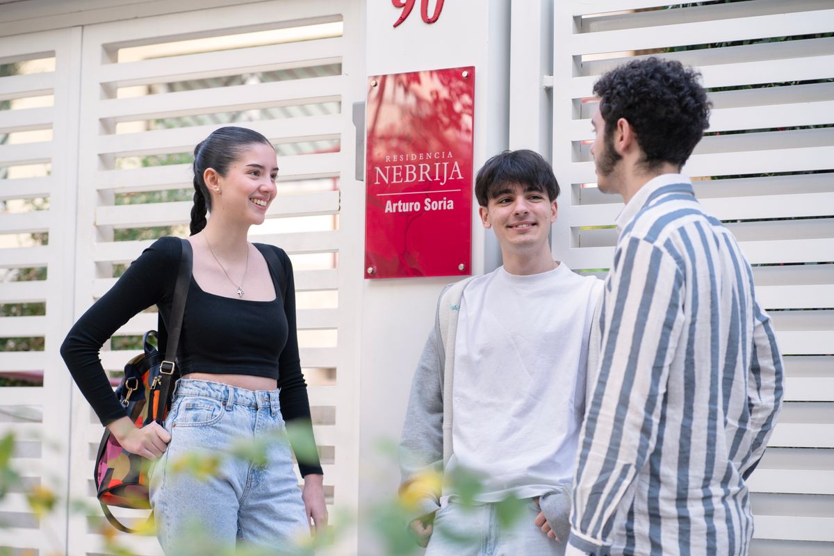 Un grupo de tres jóvenes conversan frente a una entrada con un letrero de la Universidad Nebrija.