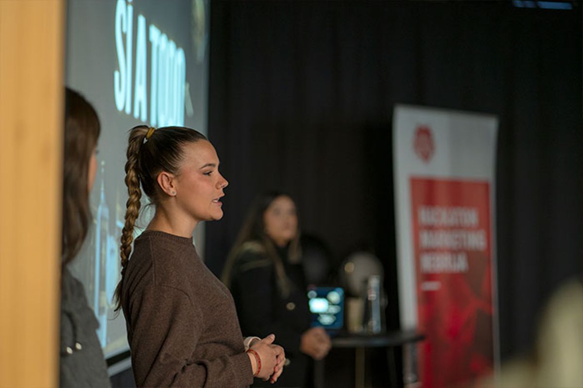 Una mujer está hablando frente a un público en un evento mientras otra persona la escucha.