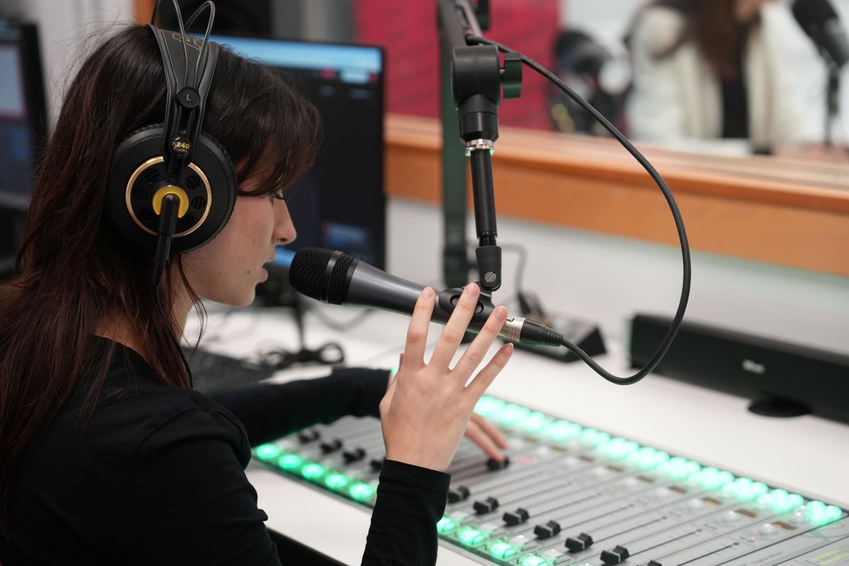 Una mujer con auriculares habla en un micrófono frente a una consola de sonido en un estudio de grabación.