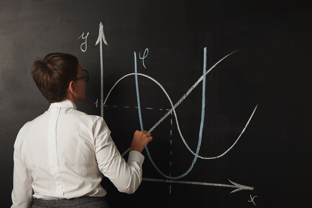 Una persona está dibujando una gráfica matemática en una pizarra con tizas de colores.