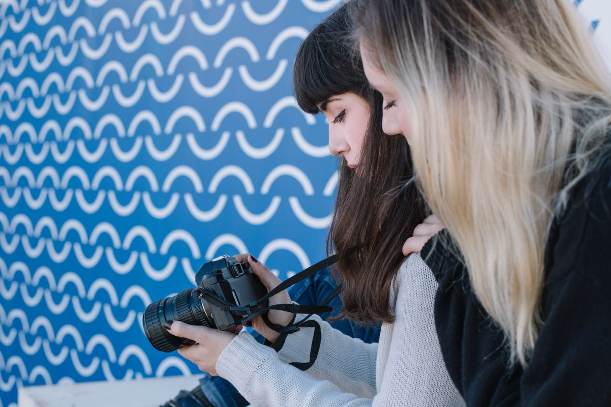 Dos personas miran una cámara en un fondo azul con un diseño ondulado.