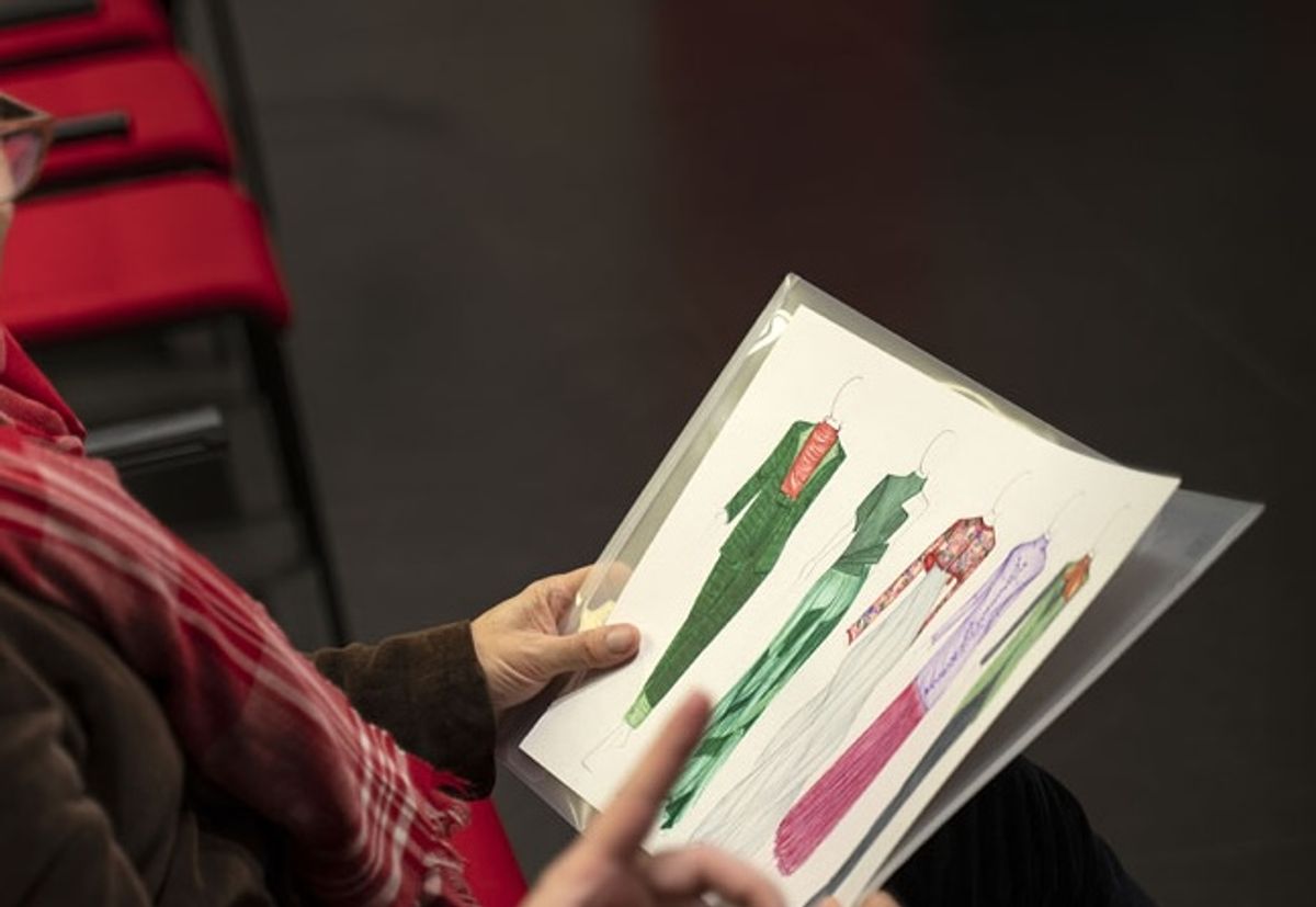 Una persona sostiene un diseño de vestidos coloridos en una reunión.