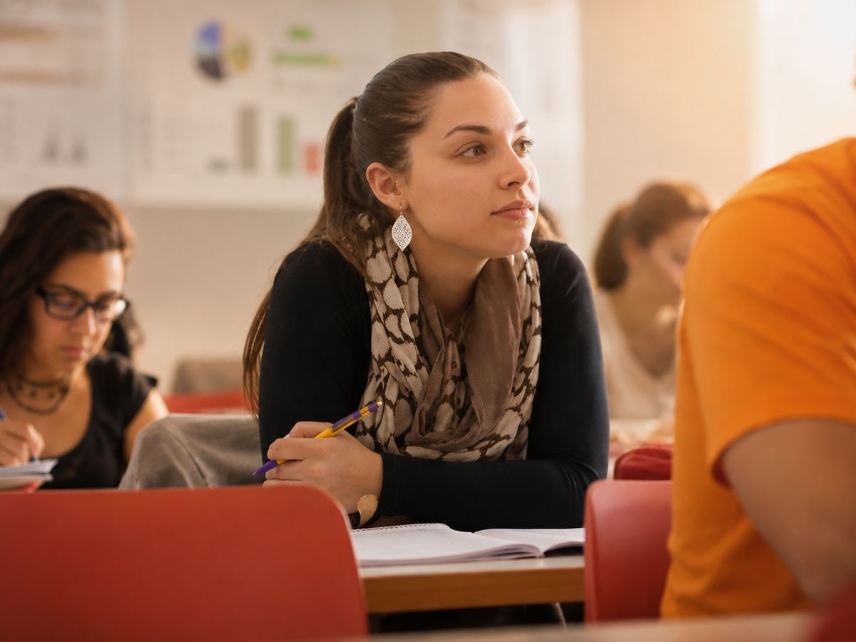 Una mujer joven está prestando atención en una clase mientras toma notas.
