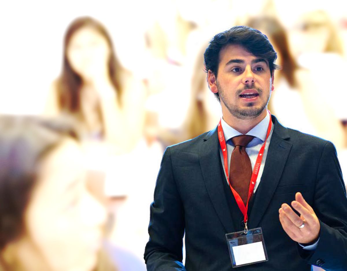 Un hombre vestido de traje habla en una conferencia frente a un público desenfocado.