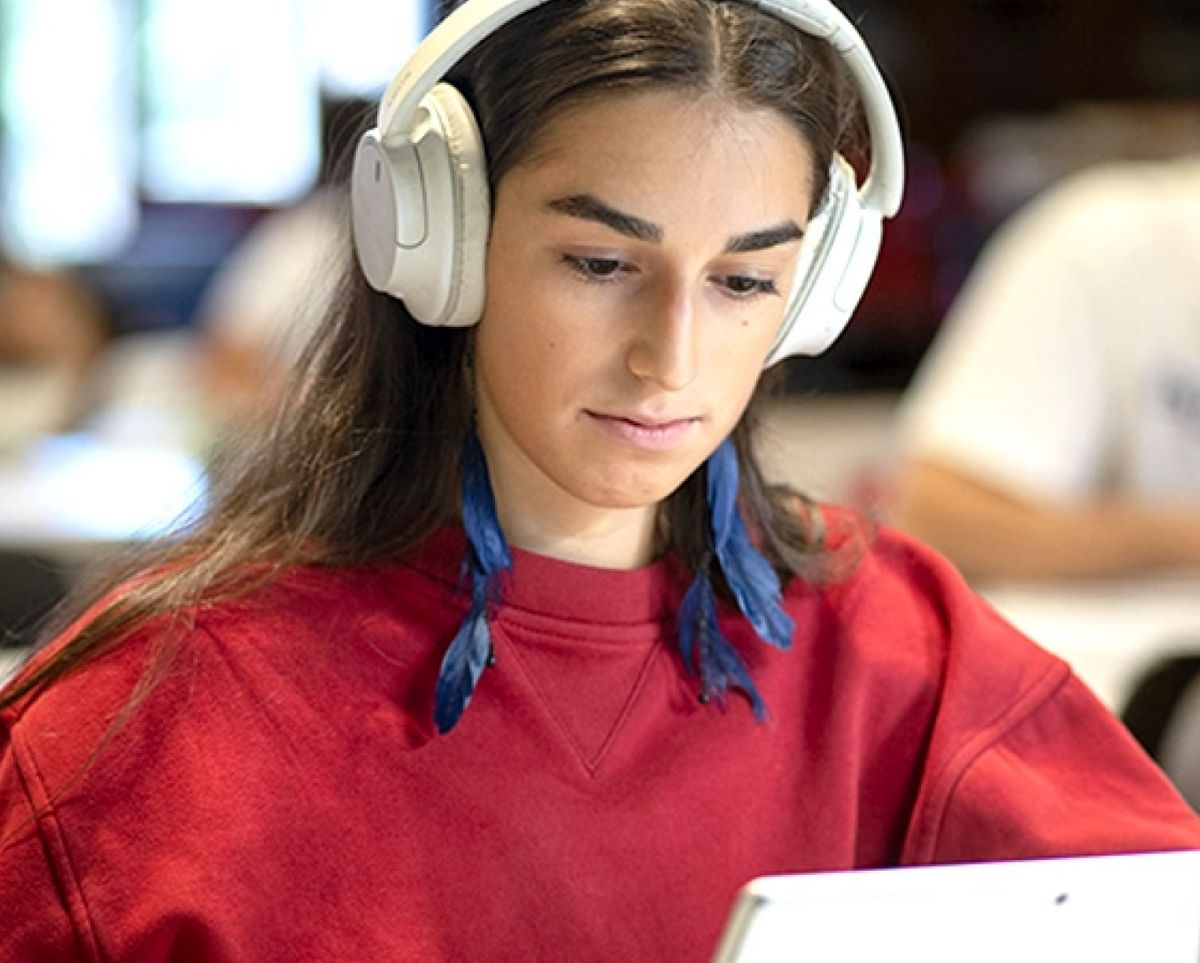 Una persona sentada con auriculares, concentrada en una tablet.