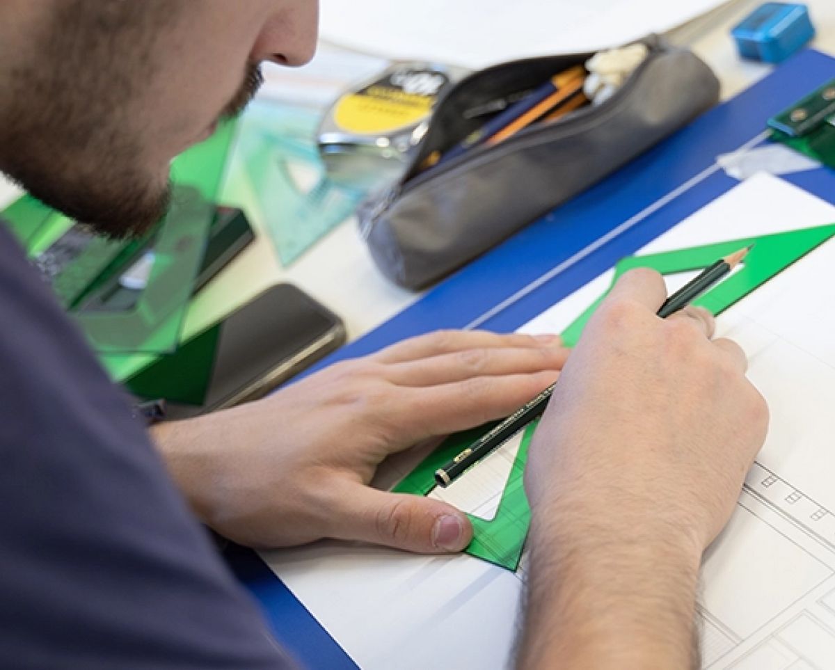 Una persona está dibujando con un lápiz sobre una hoja de papel utilizando una regla y otros útiles de oficina.