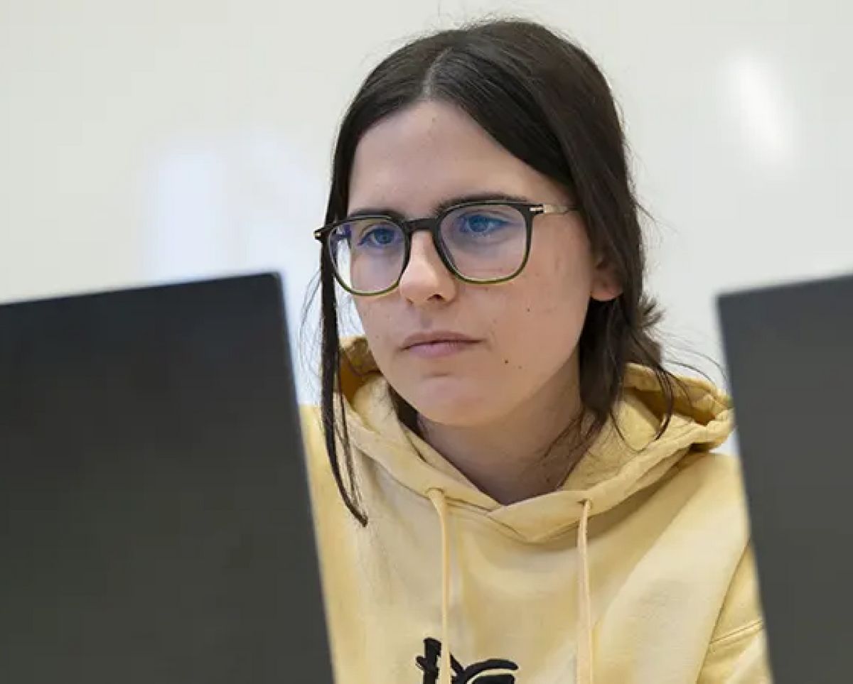 Una joven concentrada trabajando en dos computadoras portátiles.