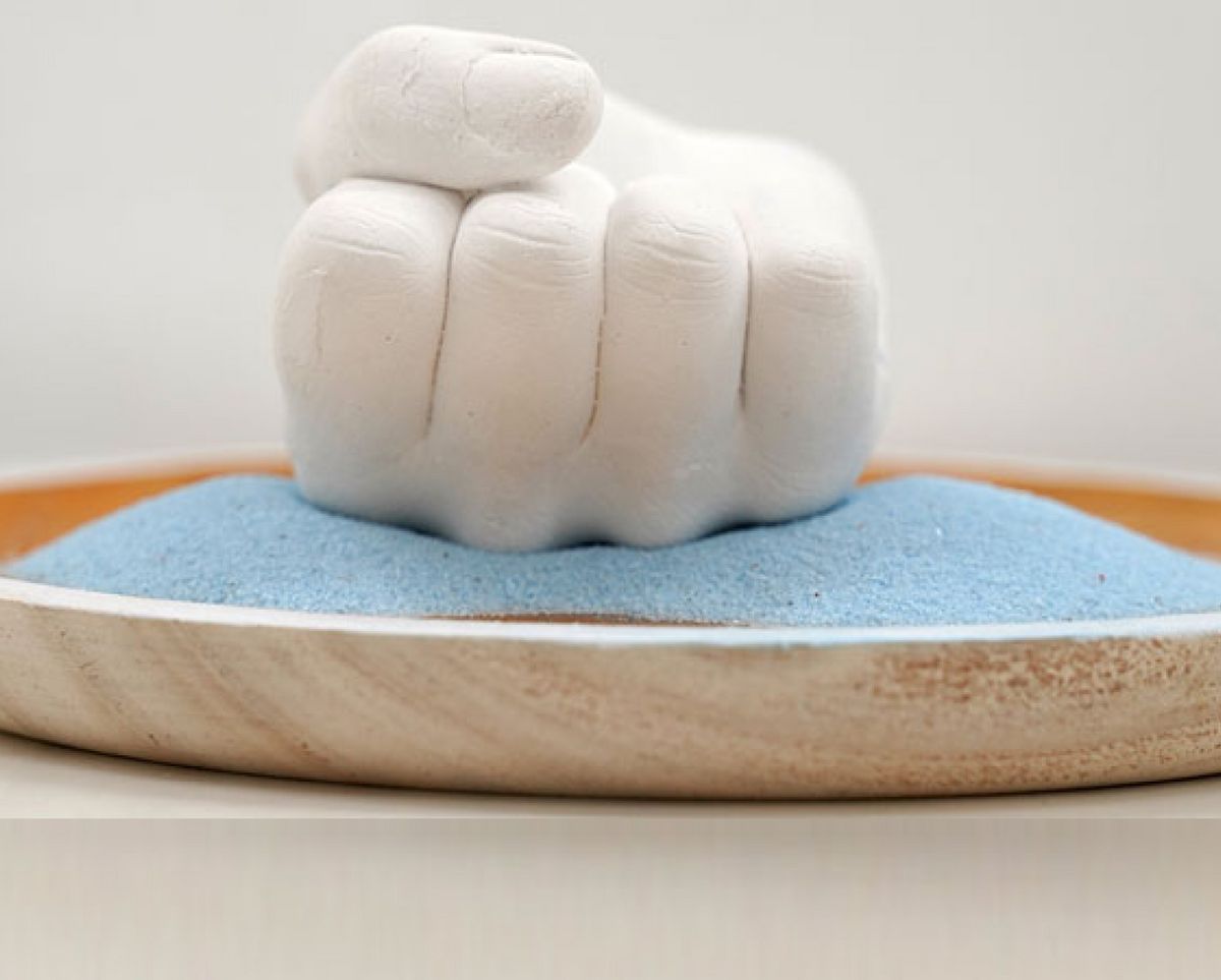 Una mano blanca en forma de puño descansa sobre arena azul en un plato de madera.