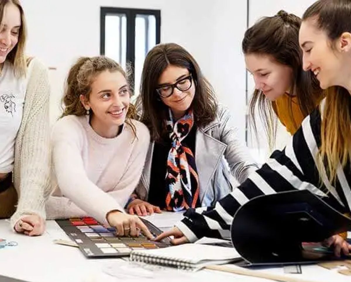 Un grupo de cinco mujeres trabaja en un proyecto creativo en una mesa, analizando muestras de color.