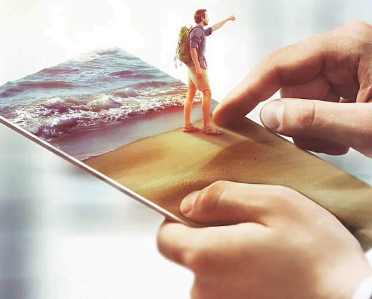 Una persona diminuta camina sobre la arena de una playa, mientras sostiene un teléfono que muestra la imagen en 3D.