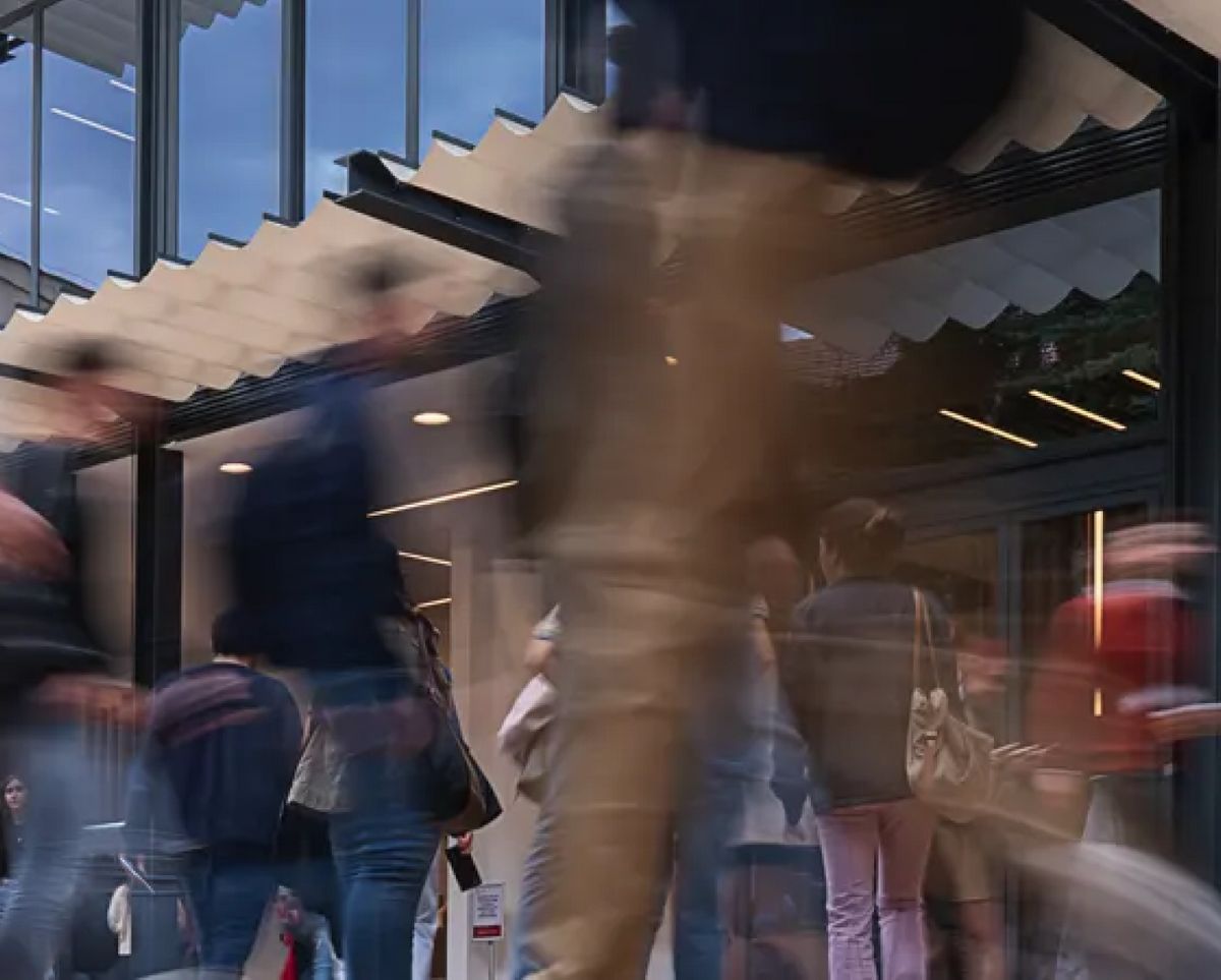 Una multitud de personas se mueve rápidamente frente a un edificio con ventanas grandes.