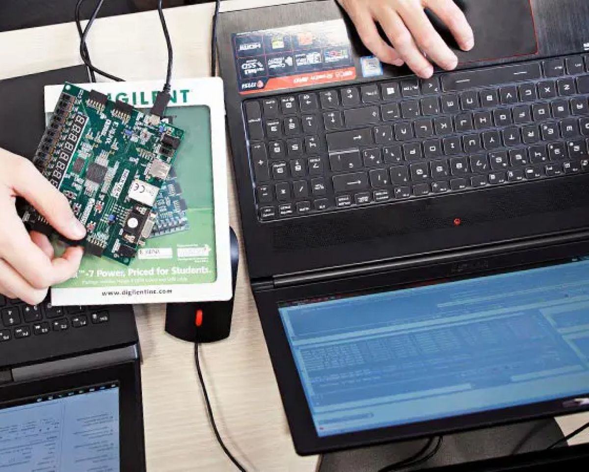 Una persona sostiene una placa de circuito mientras trabaja en dos computadoras portátiles.