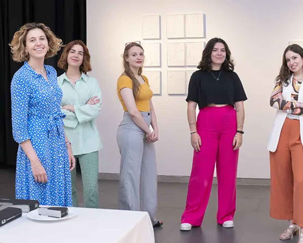 Un grupo de mujeres sonriendo en un espacio de exhibición artística.