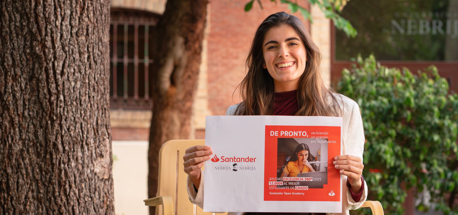 Una mujer sonriente sostiene un cartel de Santander en un entorno al aire libre.