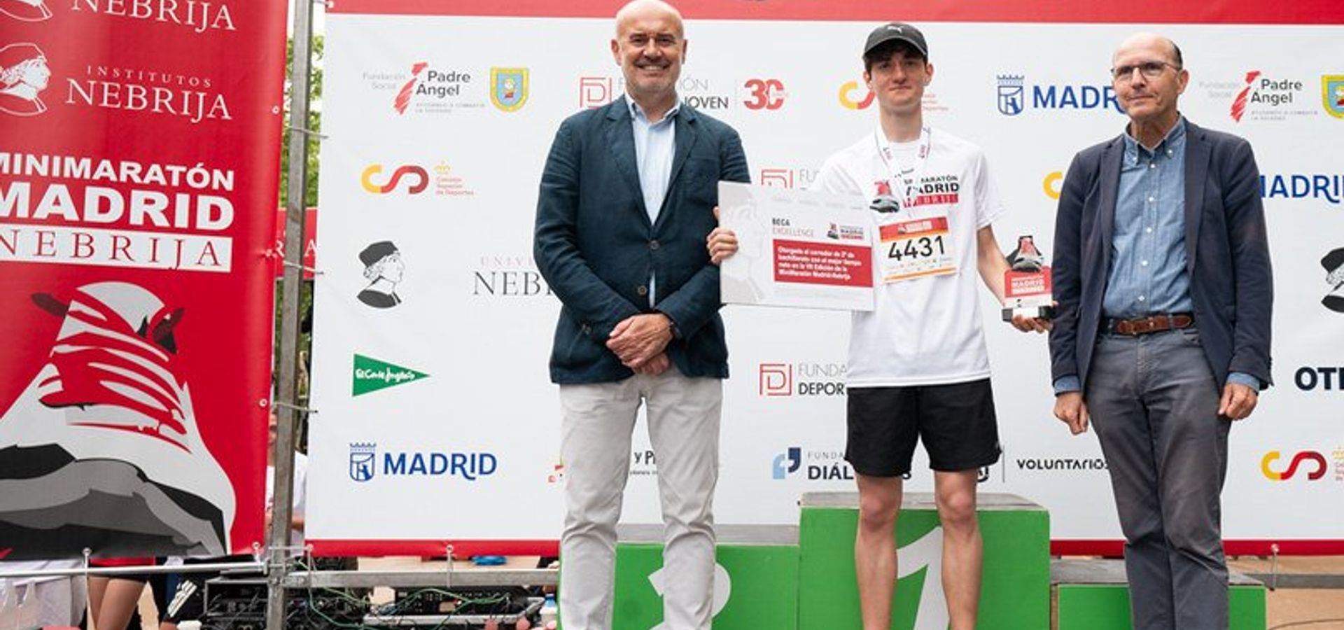Un corredor recibe un premio en la Minimarathon de Madrid, acompañado de dos personas en un escenario.