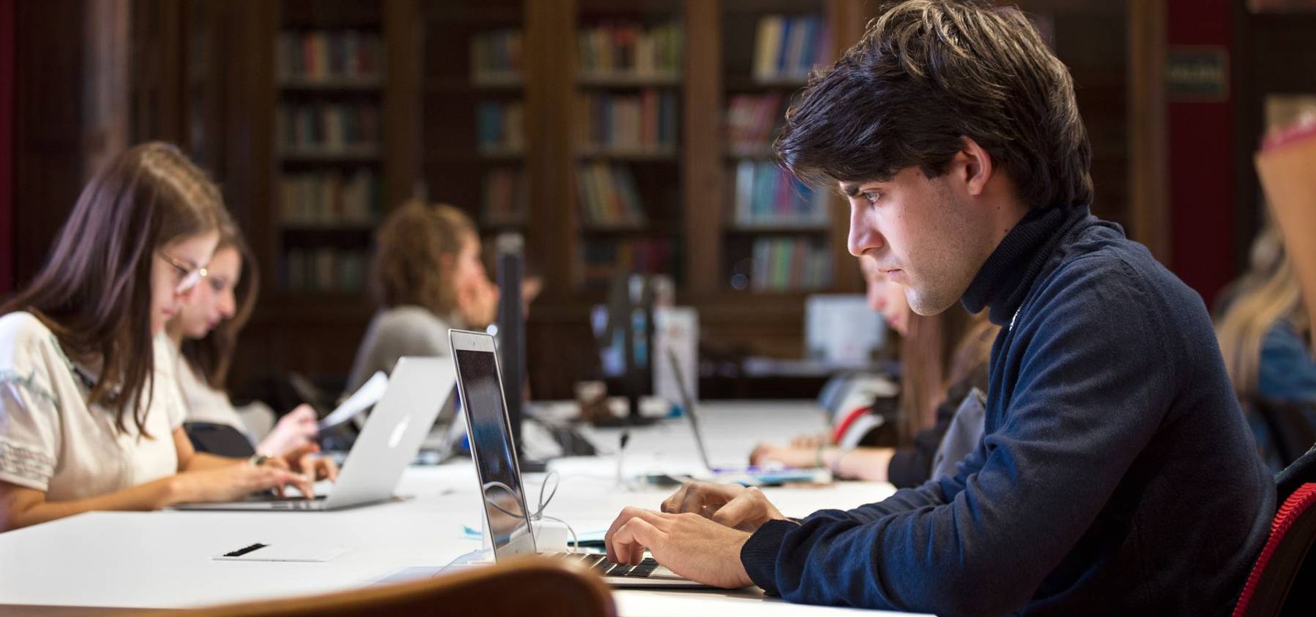 Un grupo de estudiantes trabaja en sus laptops en una biblioteca.