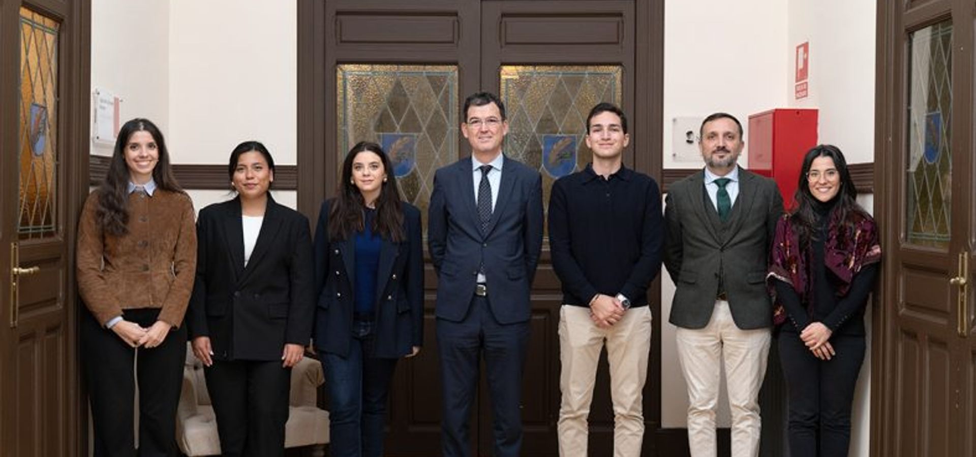 Un grupo de siete personas posando frente a una puerta con el logo de Nebrija.
