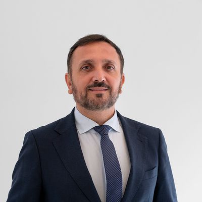 Un hombre con barba y chaqueta oscura sonríe frente a un fondo blanco.
