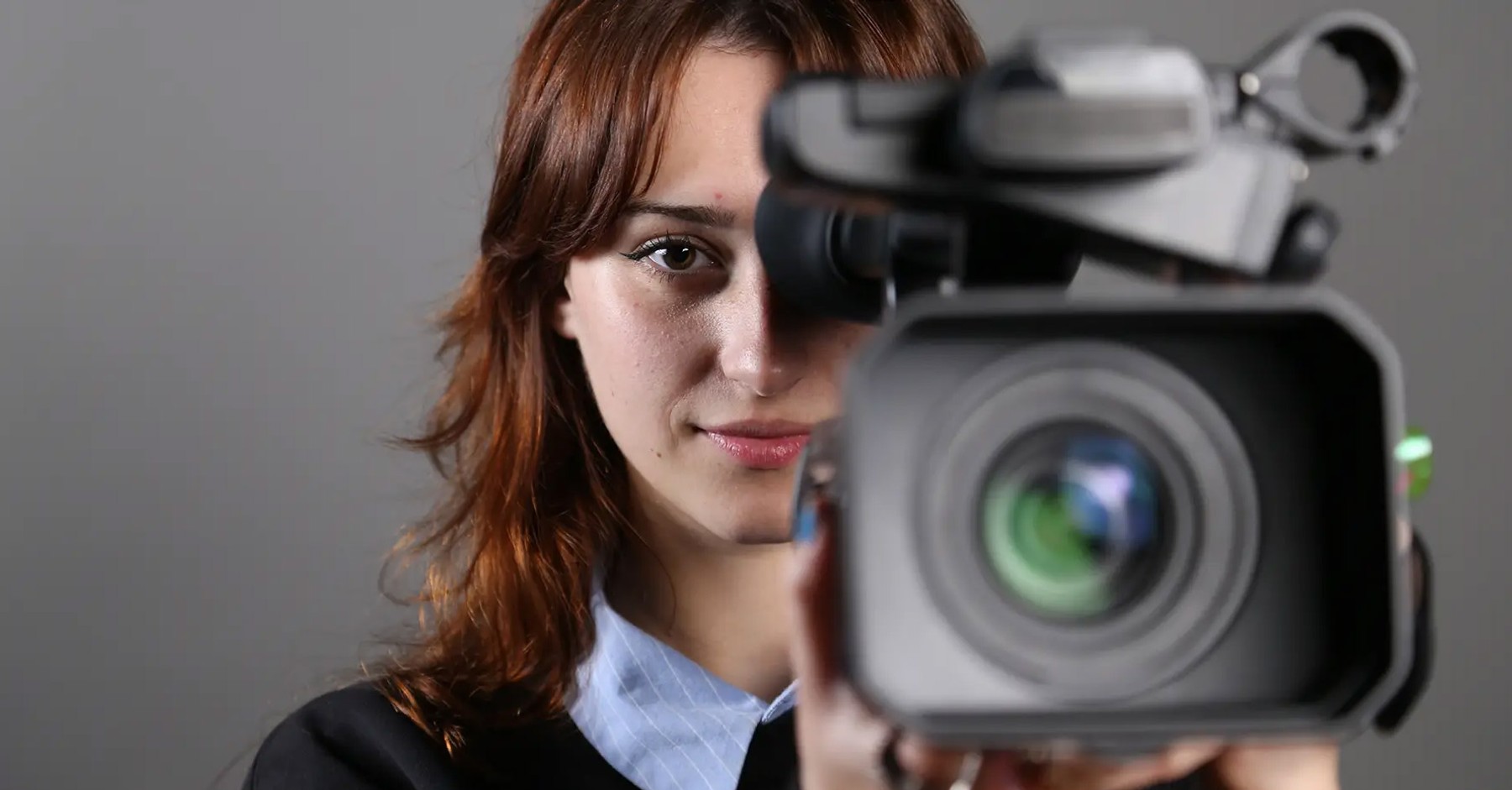 Una mujer sostiene una cámara de video mientras mira hacia la cámara.