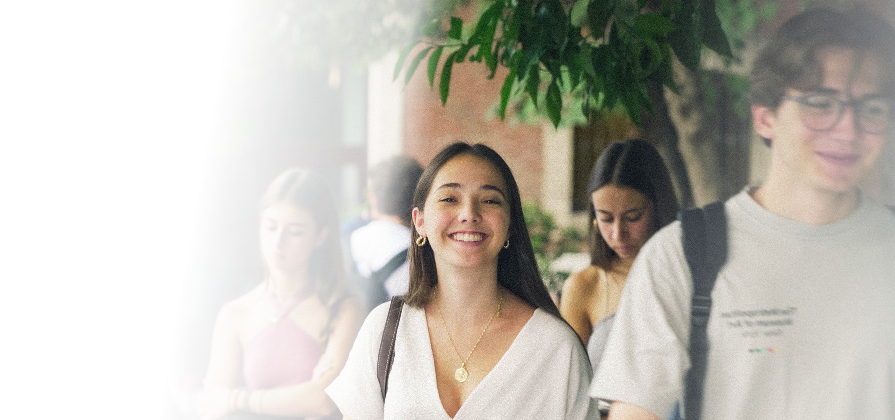 Un grupo de jóvenes camina sonriendo por la calle bajo un árbol.