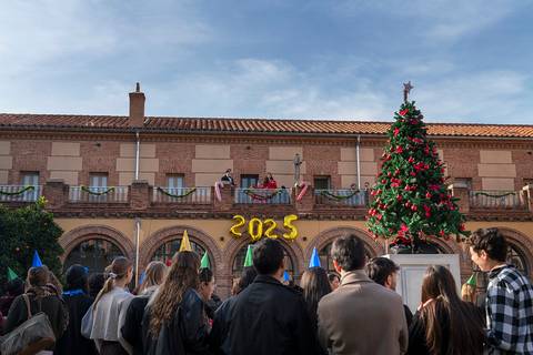 Un grupo de personas celebra la llegada del nuevo año frente a un edificio decorado con un árbol de Navidad y un letrero que dice '2025'.