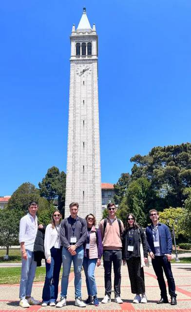 Un grupo de siete personas posando frente a una torre en un día soleado.