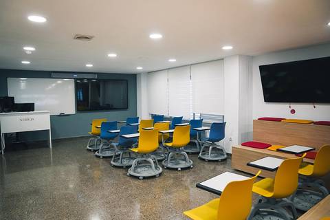 Aula moderna con sillas de colores y equipos tecnológicos.