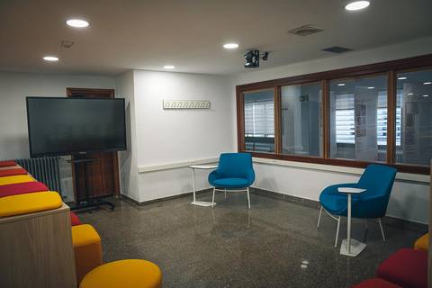 Una sala de reuniones con sillas azules y una pantalla grande en la pared.