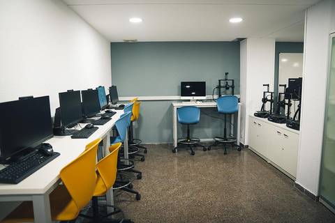 Un aula de informática con varias estaciones de trabajo y sillas coloridas.