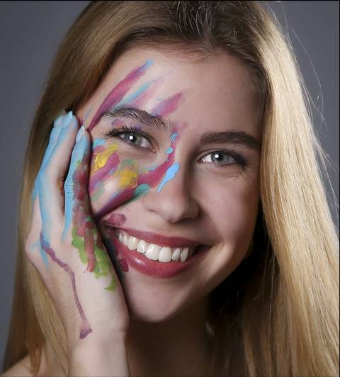 Una joven sonriente con pintura de colores en la cara y la mano.