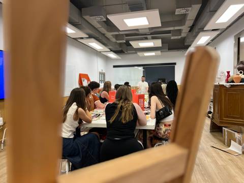 Un grupo de personas sentadas alrededor de una mesa en una sala de clases, mientras un instructor presenta al frente.