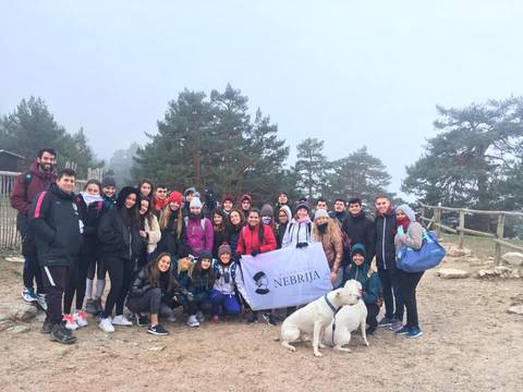 Grupo de personas sonrientes posando en un entorno natural brumoso, sosteniendo una bandera de la Universidad Nebrija.