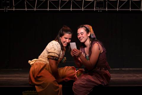 Dos mujeres sonrientes comparten un momento divertido en un escenario.