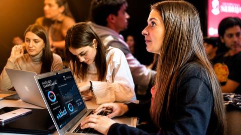 Un grupo de personas se reúne en un ambiente colaborativo, con una mujer enfocada en su laptop que muestra gráficos de análisis empresarial.