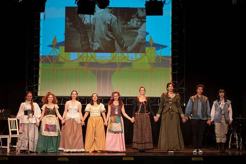 Un grupo de actores en escena se toman de las manos al finalizar una representación teatral.