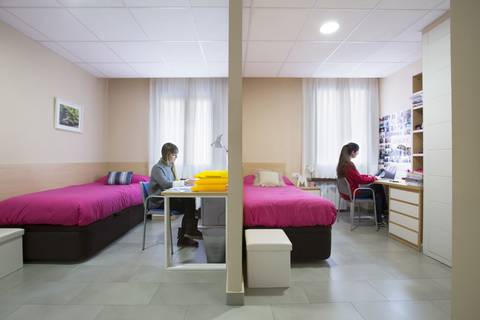 Dos estudiantes en un dormitorio compartido con camas individuales y espacios de trabajo.