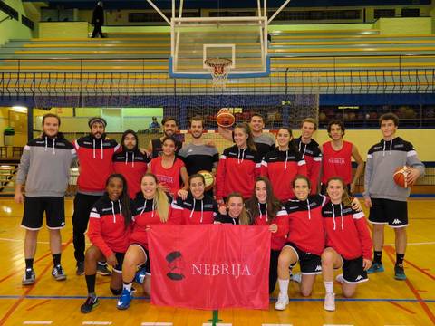 Un grupo de jugadores de baloncesto posando en una cancha con una bandera de la Universidad Nebrija.